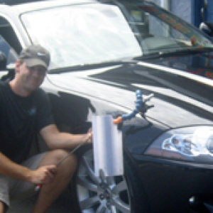 Man installing a device on a black car's hood.